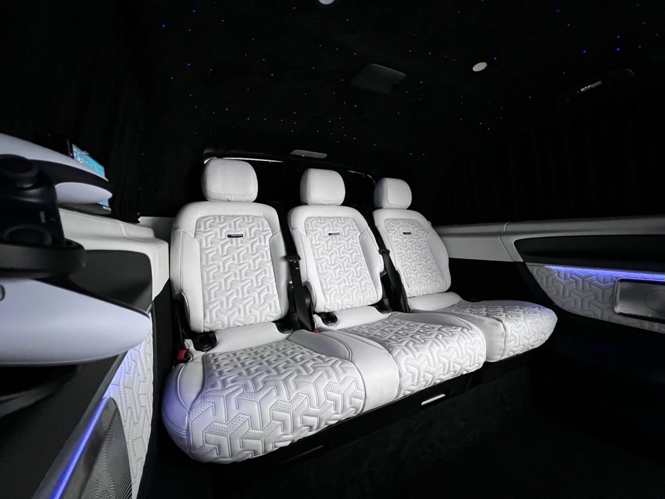 Luxurious interior of a car showing three white leather seats against a dark backdrop.